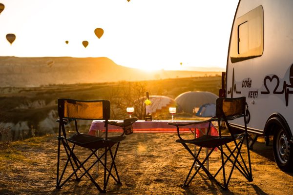 A tranquil camping setup with chairs, table, and hot air balloons in a stunning sunset view.