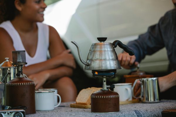 A cheerful group enjoying a hot coffee at a campsite on a sunny day, one of those glamping essentials we think is key!